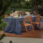 Mesa posta no jardim do Villagio Di Cedro com jogo de ceramica Buzios, jarra de vidro e prata com suco de laranja, torta de morangos num prato de bolo, uvas e petiscos variados