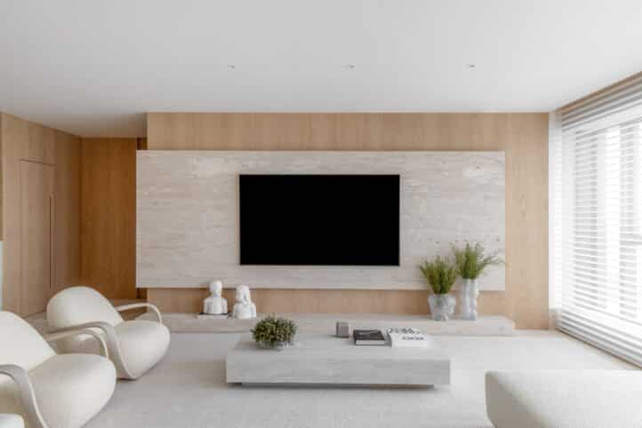 Projeto Dame Architecture de uma sala de estar com painel home theater em pedra Marmore Travertino Fosco e Móveis Claros